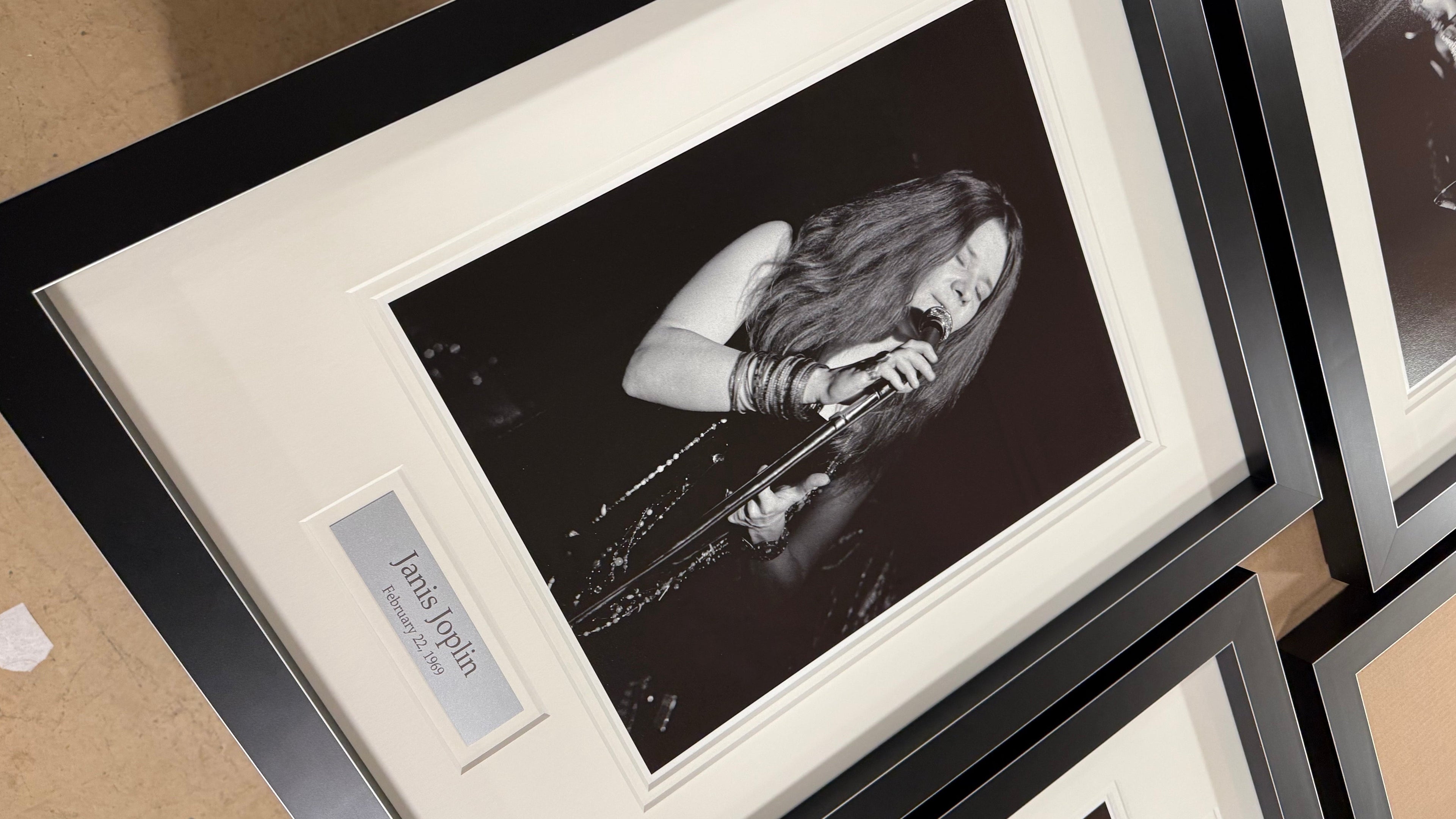 Framed black and white photograph of a person singing, with a nameplate below, on a wooden surface.